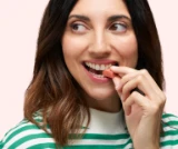 Woman in a striped shirt biting into a striped pink treat, looking to the side.